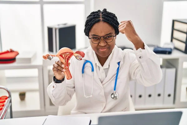 African american doctor woman holding anatomical model of female genital organ annoyed and frustrated shouting with anger, yelling crazy with anger and hand raised