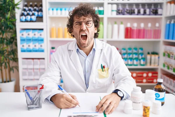 Hispanic Young Man Working Pharmacy Drugstore Angry Mad Screaming Frustrated — Stockfoto