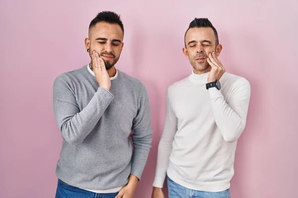 同性恋夫妇手牵手站在粉色背景上 手摸着嘴 因为牙齿疼痛或牙病而有痛苦的表情 — 图库照片