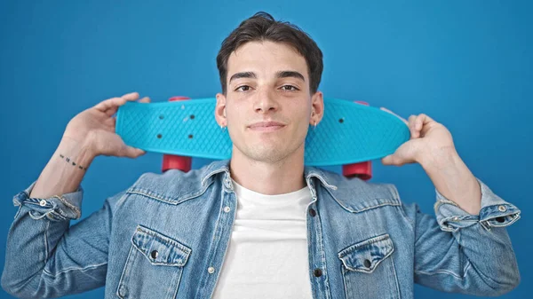 Jovem Hispânico Homem Segurando Skate Sobre Fundo Azul Isolado — Fotografia de Stock