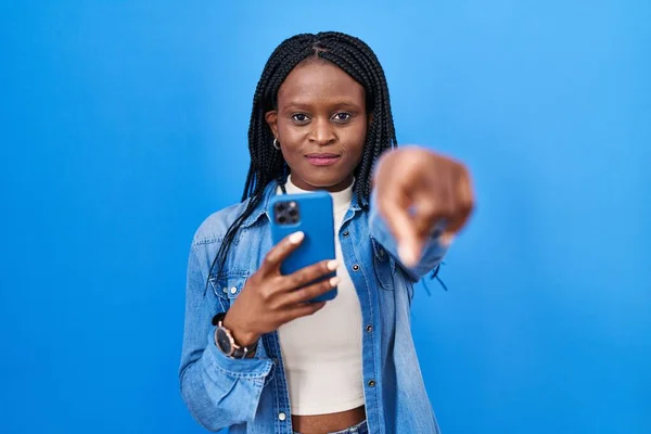 拿着辫子的非洲女人用智能手机打字 手指着相机 对着你 自信地摆出一副严肃的姿势 — 图库照片