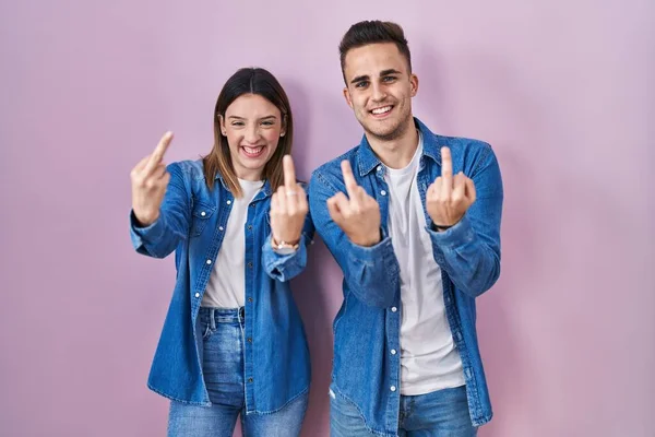 Молода Іспаномовна Пара Стоїть Над Рожевим Тлом Показуючи Середній Палець — стокове фото