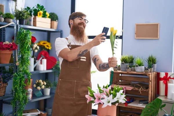 stock image Young redhead man florist make photo to flower by smartphone at flower shop