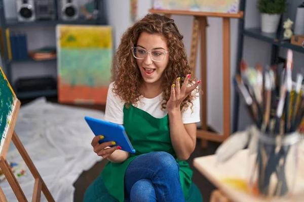 年轻的高加索女画家坐在艺术工作室里用平板电脑做视频通话 自豪地尖叫着 高举双臂庆祝胜利和成功 — 图库照片