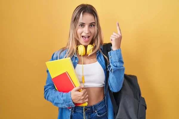 若いブロンドの女性は 学生のバックパックを着て 成功したアイデアで指を指して本を保持 興奮して幸せよ 第1位 — ストック写真