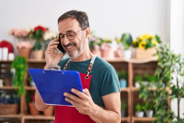 Middle age man florist talking on smartphone reading clipboard at florist