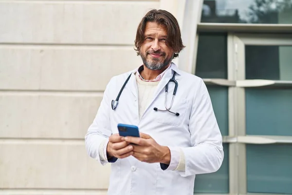 Lekarz Średnim Wieku Uśmiecha Się Pewnie Pomocą Smartfona Szpitalu — Zdjęcie stockowe