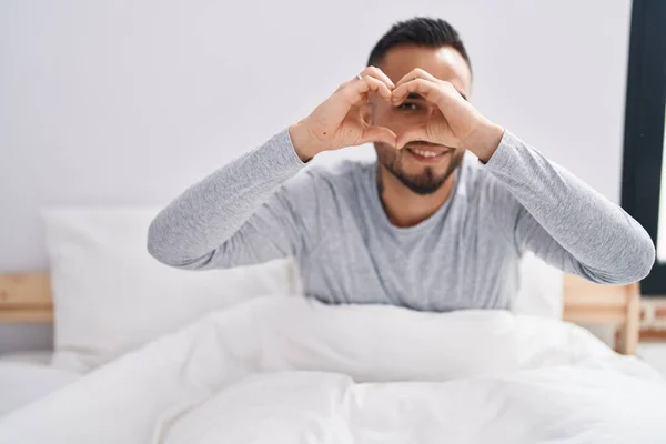 Young Hispanic Man Doing Heart Gesture Sitting Bed Bedroom — Stock fotografie