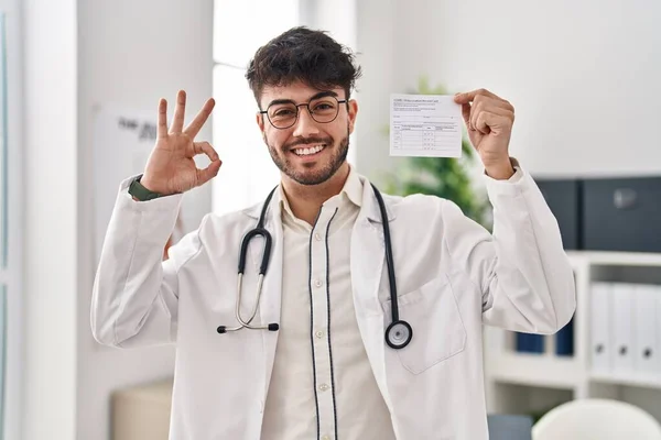 Лікар Латиноамериканець Бородою Тримає Ковальну Картку Знаком Пальців Усміхаючись Дружнім — стокове фото