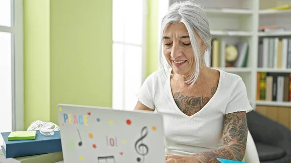 Middle age grey-haired woman student using laptop smiling at library university