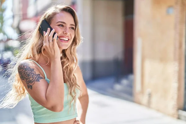 年轻的金发女人在街上用智能手机自信地微笑着 — 图库照片