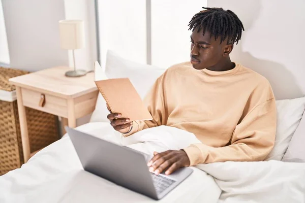 アフリカ系アメリカ人男性読書本を使用してノートパソコンでベッドルーム — ストック写真