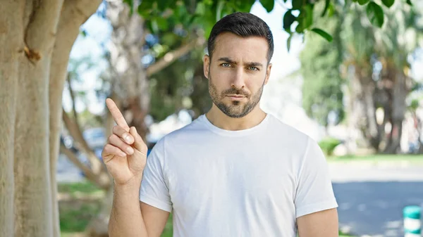 Young hispanic man standing with serious expression saying no with finger at park