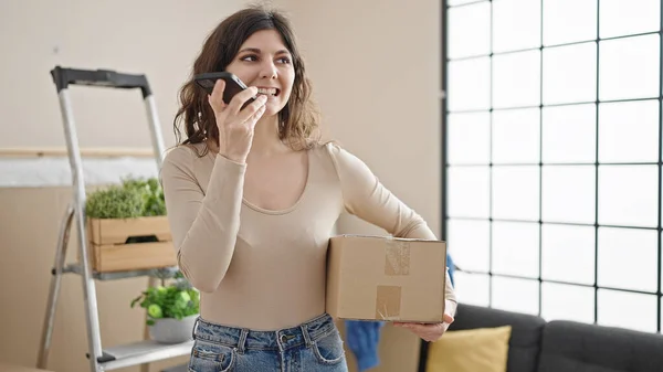 若い美しいヒスパニック女性は 新しい家でパッケージを保持スマートフォンによって音声メッセージを送信 — ストック写真