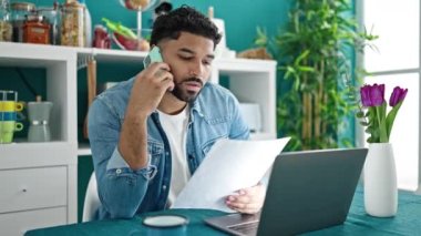 Afro-Amerikalı bir adam yemek odasında akıllı telefon okuyarak konuşuyor.