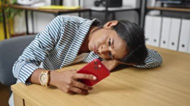Ofiste akıllı telefon kullanmaktan yorulan Afrikalı Amerikalı iş kadını.