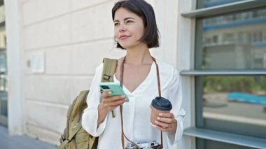 Genç ve güzel İspanyol kadın turist gülümsüyor. Akıllı telefon kullanıyor. Sokakta kahve içiyor.