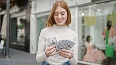 Young blonde woman smiling confident counting dollars at street