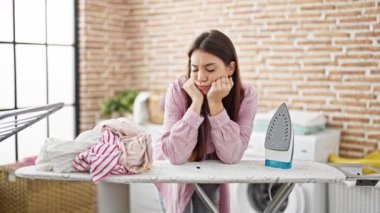 Genç ve güzel İspanyol kadın çamaşırhanede üzgün bir ifadeyle ütü masasına yaslanıyor.