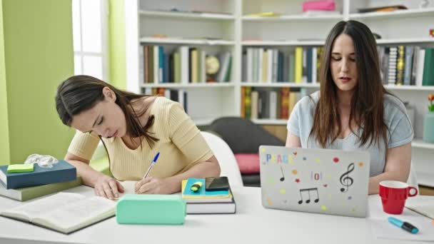 Two Women Sitting Table Studying Using Laptop Writing Notes Library — Stock Video