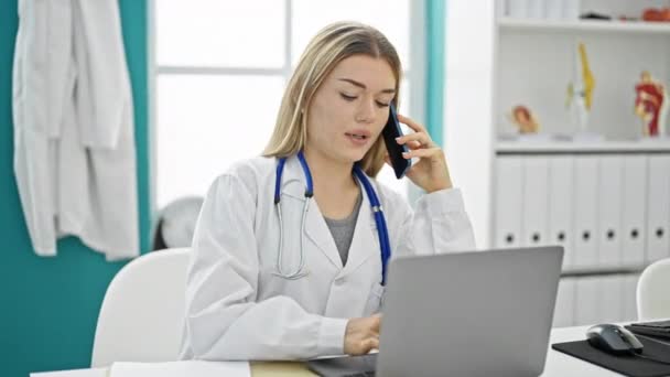 Young Blonde Woman Doctor Using Laptop Talking Smartphone Clinic — Stock Video