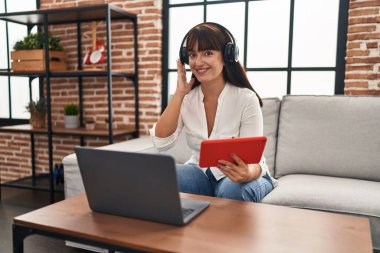 Genç, güzel, İspanyol bir kadın evdeki kanepede oturmuş müzik dinliyor.