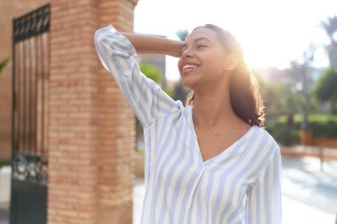 Young african american woman smiling confident relaxed with hand on head at street