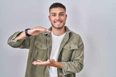 İzole edilmiş arka planda duran genç İspanyol adam. Elleriyle büyük ve büyük bir işaret, ölçü sembolü gösteriyor. Kameraya bakıp gülümsüyor. ölçüm kavramı. 