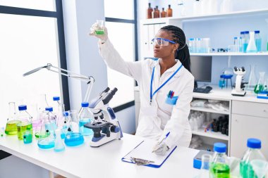 African american woman scientist holding test tube writing report at laboratory