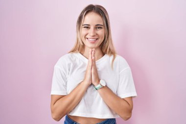 Pembe arka planda duran genç sarışın kadın ellerini birleştirip af diliyor kendinden emin bir şekilde gülümseyerek.. 