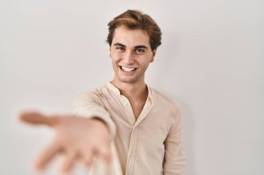 Young man standing over isolated background smiling cheerful offering palm hand giving assistance and acceptance. 