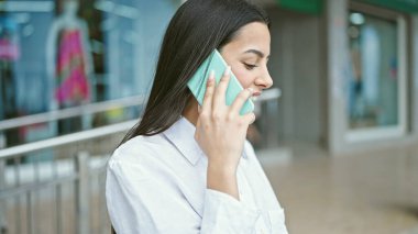 Genç, güzel İspanyol bir kadın akıllı telefondan konuşuyor. Sokakta gülümsüyor.