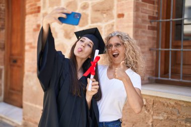 İki kadın anne ve mezun kız kampüs üniversitesinde akıllı telefondan selfie çekiyorlar.