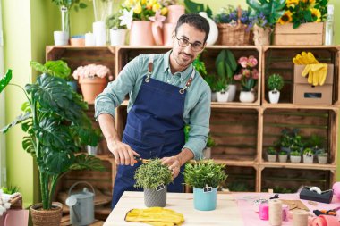 Young hispanic man florist cutting plant at flower shop