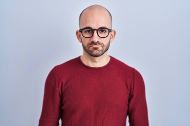 Beyaz arka planda duran sakallı genç kel adam gözlük takıyor ve yüzünde ciddi bir ifadeyle rahatlıyor. Basit ve doğal bir şekilde kameraya bakıyorsun.. 