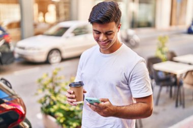 Genç İspanyol adam akıllı telefon kullanıyor, sokakta kahve içiyor.