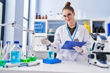 Young woman scientist reading document measuring liquid at laboratory