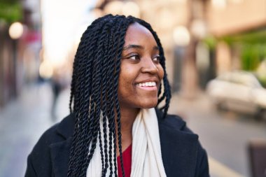 Afro-Amerikalı kadın gülümsüyor. Kendinden emin bir şekilde caddeye bakıyor.