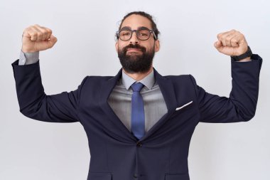 Hispanic man with beard wearing suit and tie showing arms muscles smiling proud. fitness concept. 