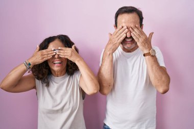 Orta yaşlı İspanyol çift pembe arka planda birlikte. Gözleri kapatıyorlar. Gülümseyen neşeli ve komik eller. kör kavram. 