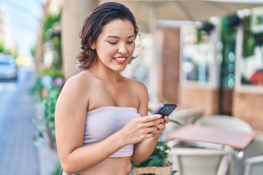 Young hispanic woman smiling confident using smartphone at coffee shop terrace