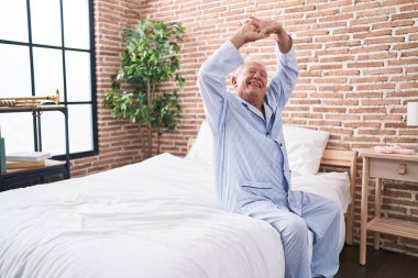 Middle age grey-haired man waking up stretching arms at bedroom