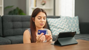 Genç ve güzel İspanyol bir kadın elinde kredi kartıyla evde oturuyor.