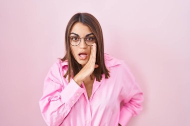 Genç İspanyol kadın, pembe arka planda duran gözlüklü, ağzı açık, gizli dedikodular söyleyen, kötü niyetli konuşmalar fısıldayan. 