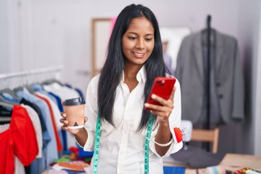 Terzide kahve içen akıllı telefon kullanan genç ve güzel bir kadın.