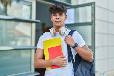 Young hispanic teenager student smiling confident holding books at university