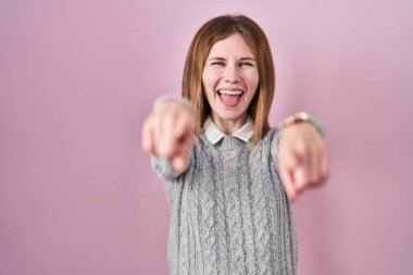 Pembe arka planda duran güzel bir kadın sana ve kameraya parmaklarıyla bakıyor, gülümsüyor pozitif ve neşeli. 