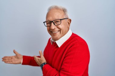 Senior man with grey hair standing over isolated background inviting to enter smiling natural with open hand 