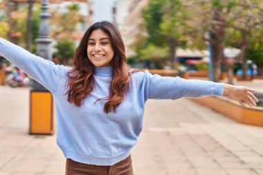 Young hispanic woman smiling confident standing with open arms at park