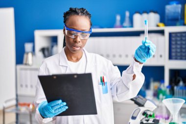 African american woman scientist holding test tube reading document at laboratory